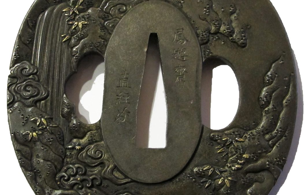Tsuba en shibuichi de forme nagamarugata, ciselée en takaniku bori et incrustée en ten zogan, uttori zogan or, illustrant la légende de la pénitence de Mongaku